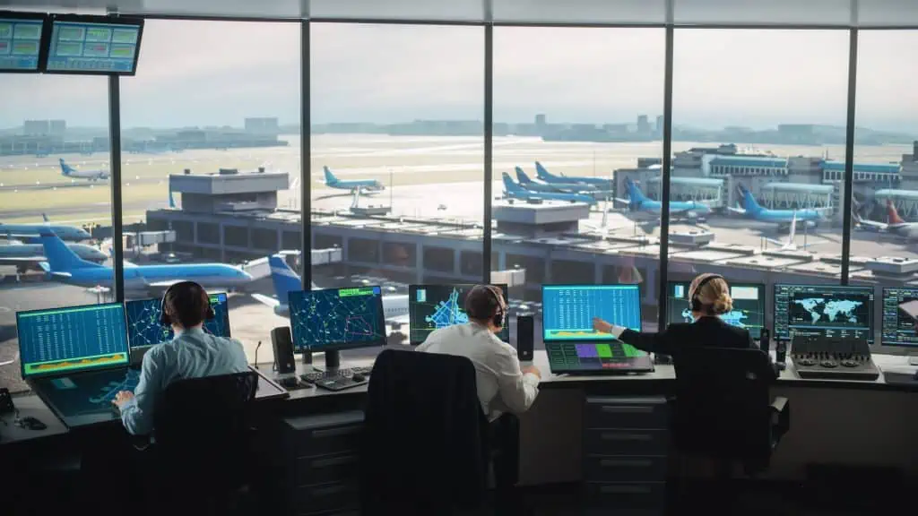 Three air traffic controllers sitz in front of their computer screens at their desks in an airport tower and control room. IHSE KVM systems ensure the direct transmission of mission critical data to airport towers for a smooth airport operation and secure air traffic.