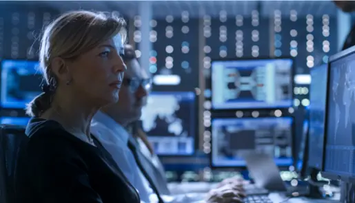 Blond woman with low ponytail and male colleague with glasses working in a control room